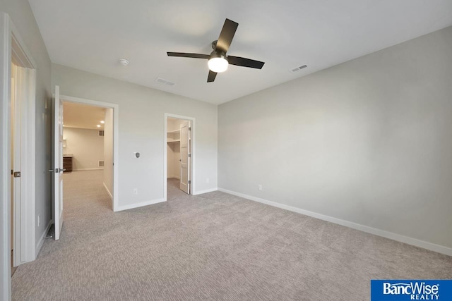 unfurnished bedroom featuring light colored carpet, a walk in closet, ceiling fan, and a closet