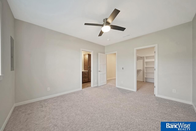 unfurnished bedroom featuring light colored carpet, ceiling fan, a walk in closet, and ensuite bathroom