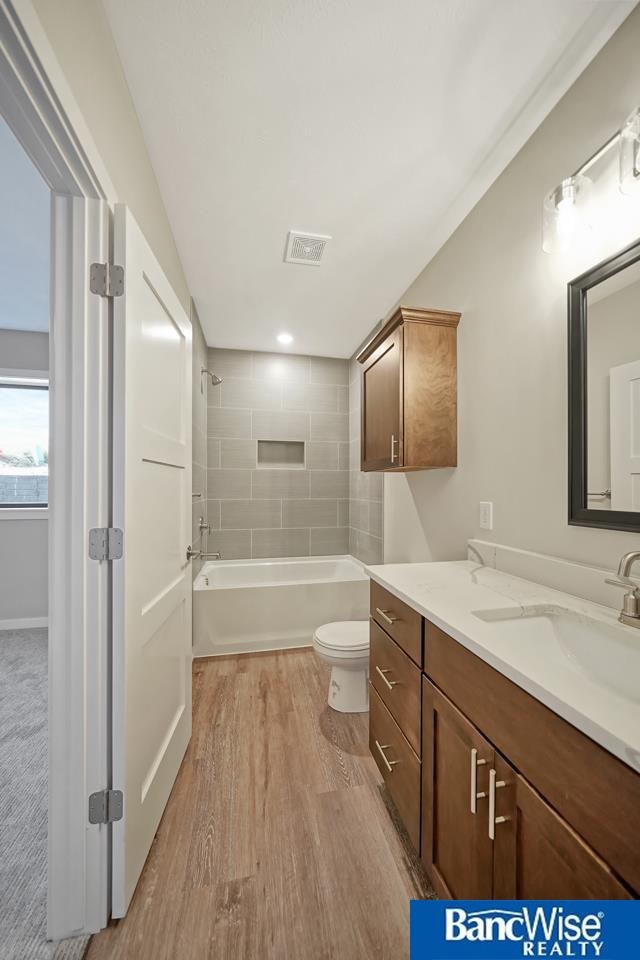 full bathroom with tiled shower / bath, vanity, hardwood / wood-style flooring, and toilet