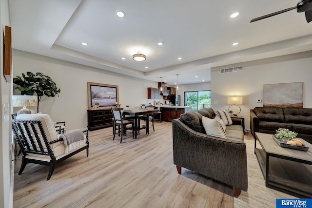 living room with light hardwood / wood-style floors and a tray ceiling