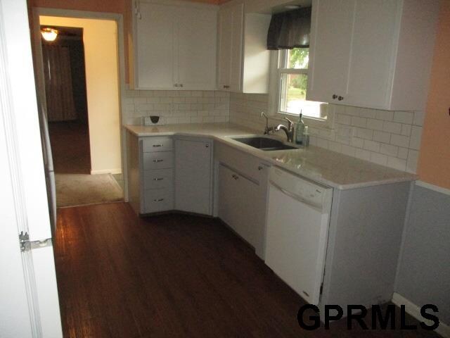 kitchen with backsplash, white dishwasher, white cabinetry, sink, and dark wood-type flooring