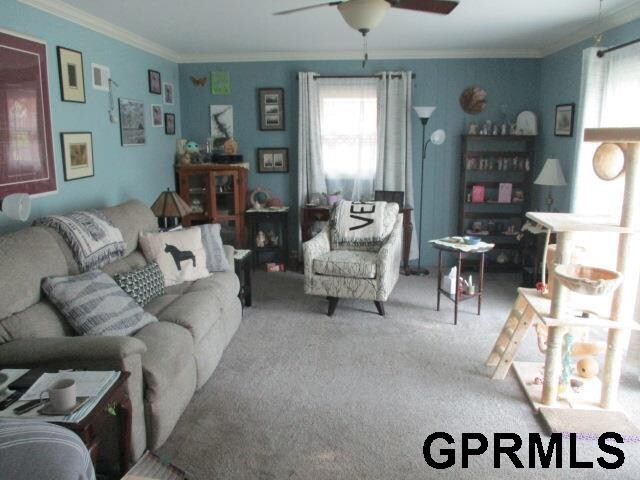 carpeted living room featuring crown molding and ceiling fan