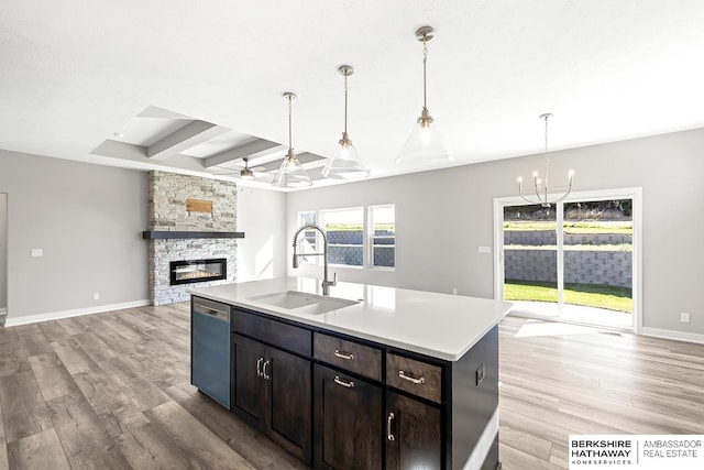 kitchen with a stone fireplace, dishwasher, light wood-type flooring, a center island with sink, and sink