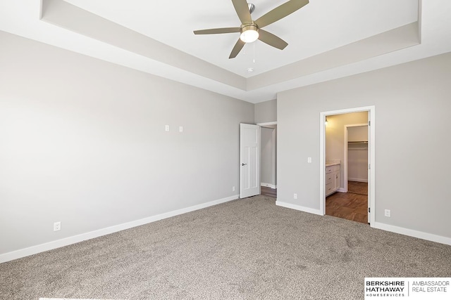 unfurnished bedroom featuring a walk in closet, ceiling fan, a raised ceiling, and carpet floors