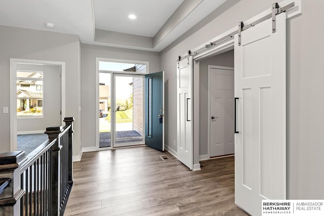 entryway with a barn door, a raised ceiling, and light hardwood / wood-style flooring