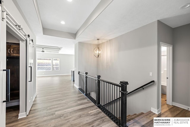 corridor with a barn door, a textured ceiling, light hardwood / wood-style flooring, and a notable chandelier