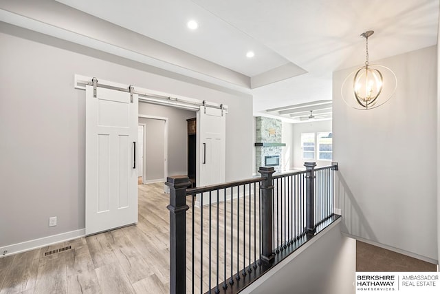 hall featuring a barn door, light wood-type flooring, and an inviting chandelier