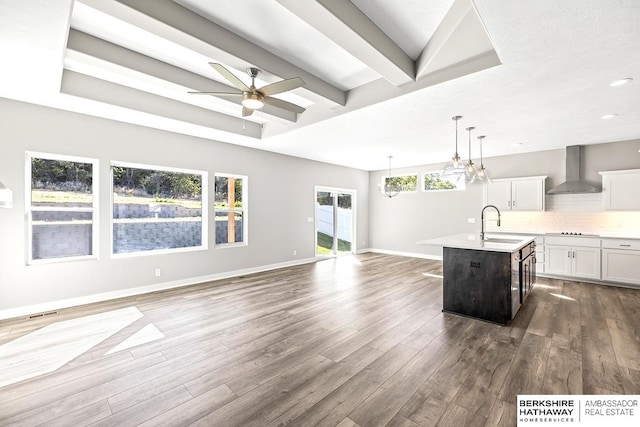 kitchen with a center island with sink, dark hardwood / wood-style floors, wall chimney range hood, and decorative light fixtures