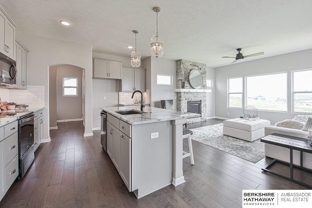 kitchen with backsplash, a stone fireplace, electric range, a kitchen island with sink, and dark hardwood / wood-style floors