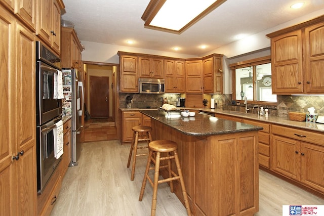 kitchen with tasteful backsplash, appliances with stainless steel finishes, light hardwood / wood-style floors, and a kitchen island