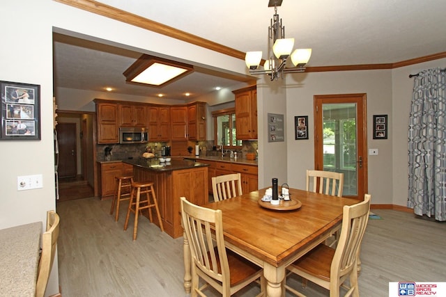 dining area featuring sink, a chandelier, light hardwood / wood-style flooring, and ornamental molding