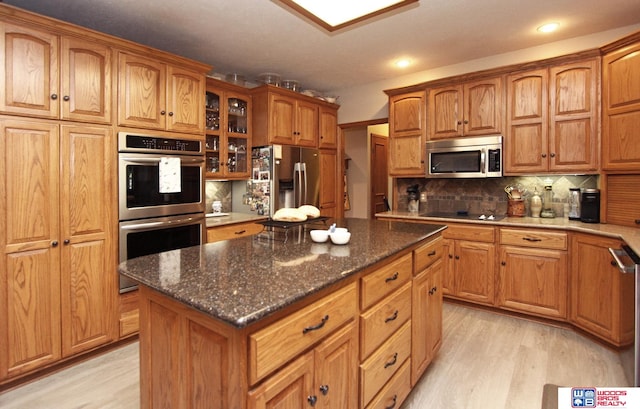 kitchen with tasteful backsplash, stainless steel appliances, light wood-type flooring, dark stone countertops, and a kitchen island