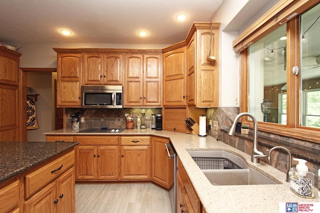 kitchen featuring stainless steel appliances, light stone countertops, backsplash, and light wood-type flooring