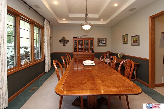 carpeted dining space with a raised ceiling