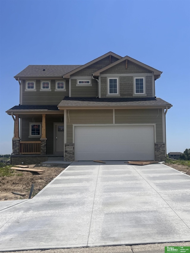 craftsman-style house featuring a garage, concrete driveway, covered porch, and stone siding