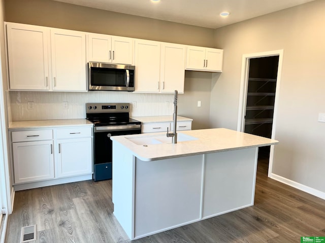 kitchen with tasteful backsplash, a kitchen island with sink, white cabinets, and appliances with stainless steel finishes