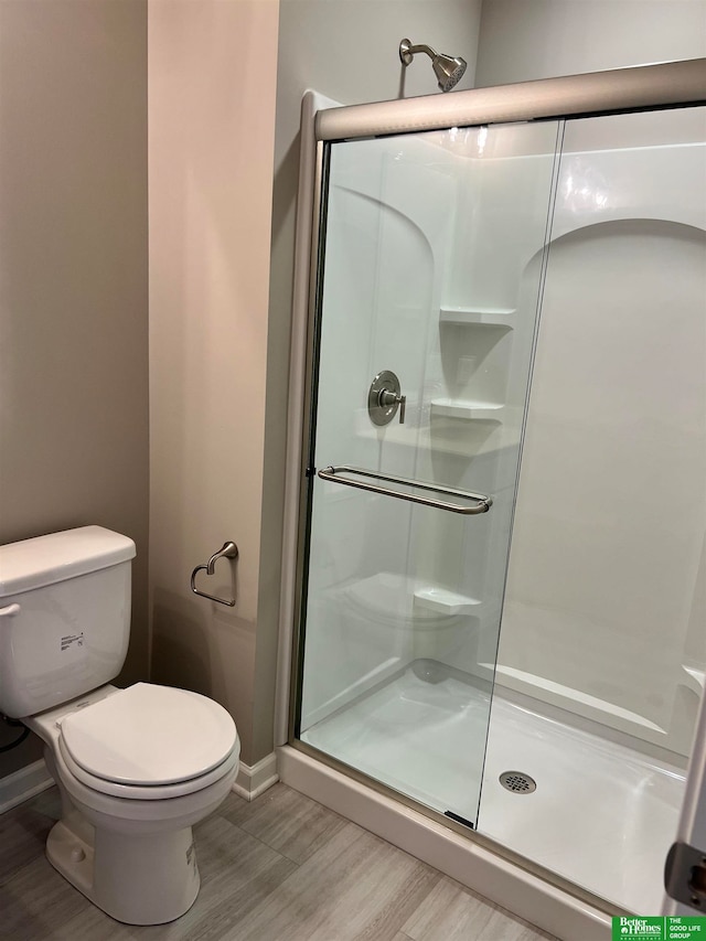 bathroom with hardwood / wood-style floors, toilet, and a shower with shower door