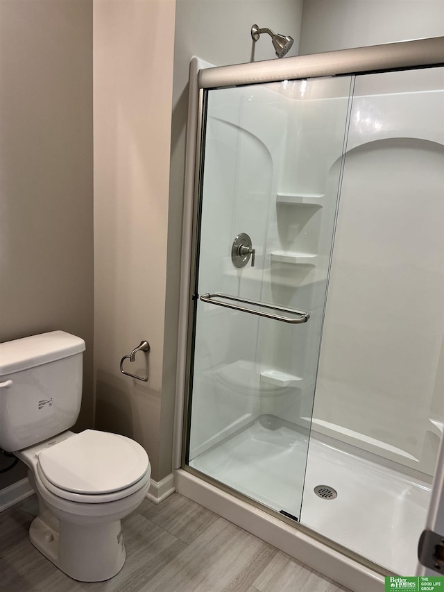 full bath with a shower stall, wood finished floors, toilet, and baseboards