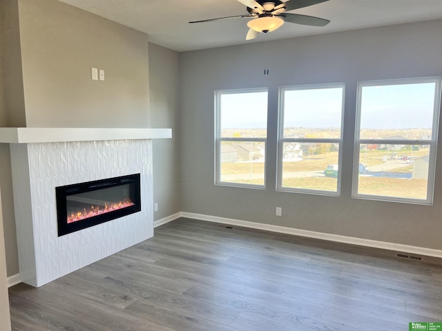 unfurnished living room with a glass covered fireplace, ceiling fan, wood finished floors, and baseboards