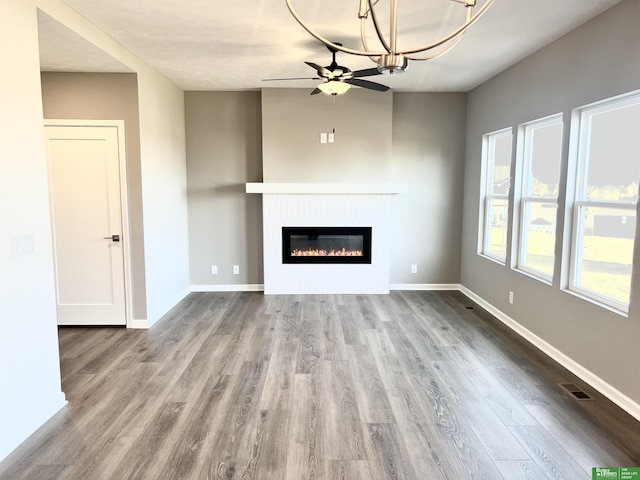 unfurnished living room featuring a glass covered fireplace, ceiling fan, wood finished floors, and baseboards