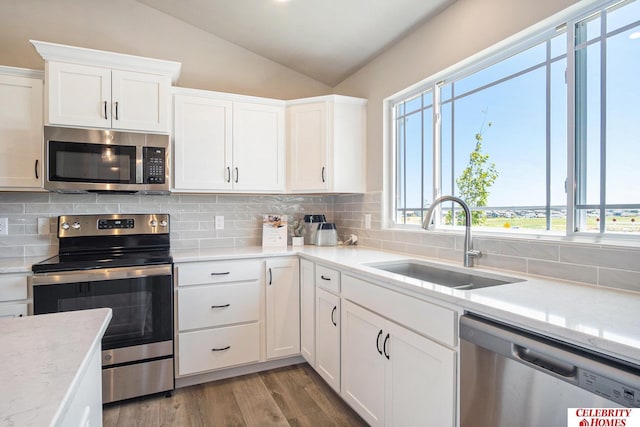 kitchen with white cabinetry, sink, stainless steel appliances, backsplash, and vaulted ceiling