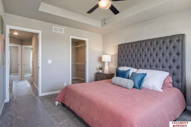 bedroom featuring a walk in closet, a tray ceiling, ceiling fan, dark colored carpet, and a closet