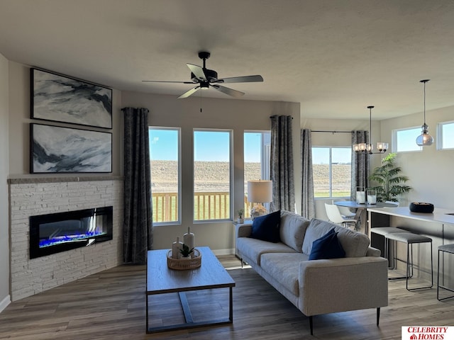 living room featuring ceiling fan with notable chandelier, a stone fireplace, and wood-type flooring