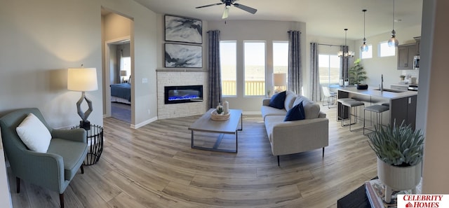 living room featuring ceiling fan with notable chandelier, sink, a fireplace, and light hardwood / wood-style flooring