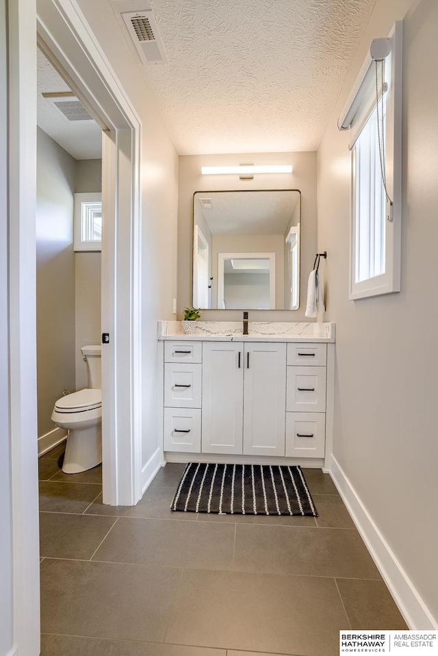 bathroom featuring a textured ceiling, toilet, tile patterned flooring, and vanity