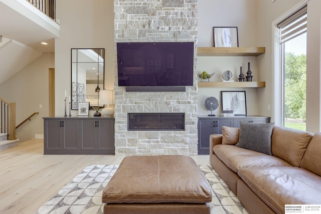 living room featuring lofted ceiling, a healthy amount of sunlight, a stone fireplace, and light hardwood / wood-style floors