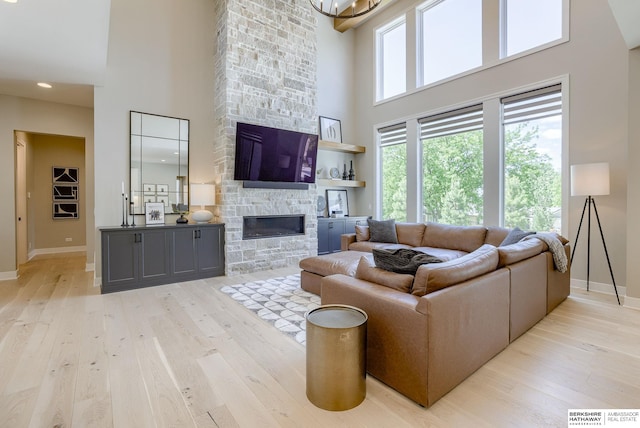 living room with a towering ceiling, a stone fireplace, and light hardwood / wood-style floors