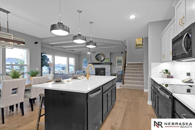 kitchen with light hardwood / wood-style floors, backsplash, white cabinetry, a stone fireplace, and sink