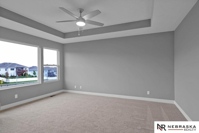 carpeted spare room with a raised ceiling and ceiling fan