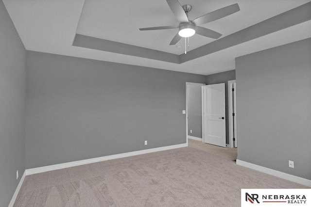 carpeted empty room with ceiling fan and a tray ceiling