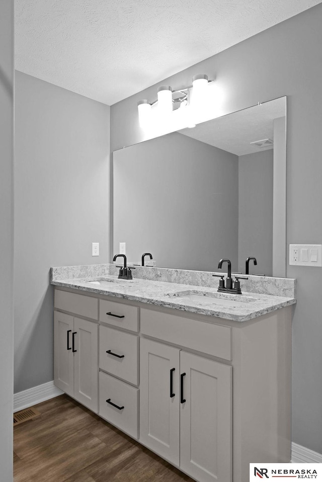 bathroom with dual bowl vanity, a textured ceiling, and hardwood / wood-style flooring