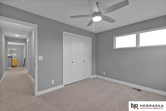 unfurnished bedroom featuring carpet flooring, a closet, and ceiling fan with notable chandelier