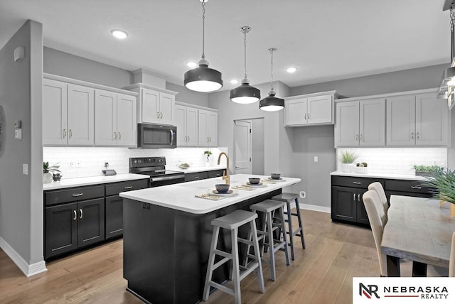 kitchen featuring an island with sink, light hardwood / wood-style flooring, tasteful backsplash, and stainless steel range with electric cooktop