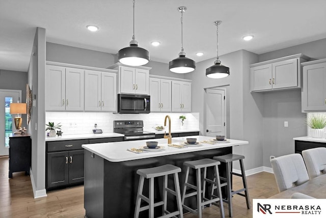 kitchen with an island with sink, light wood-type flooring, backsplash, white cabinetry, and appliances with stainless steel finishes