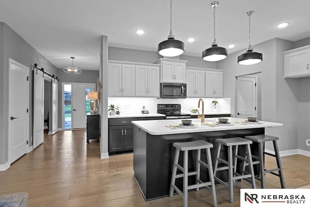 kitchen with light wood-type flooring, appliances with stainless steel finishes, white cabinets, a barn door, and tasteful backsplash