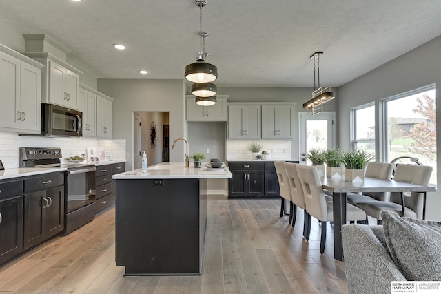 kitchen featuring hanging light fixtures, light hardwood / wood-style flooring, stainless steel electric stove, a kitchen island with sink, and white cabinets