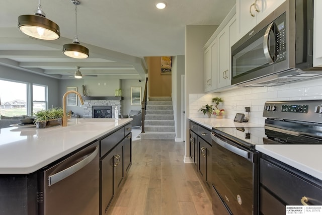 kitchen with pendant lighting, light hardwood / wood-style floors, beam ceiling, white cabinetry, and stainless steel appliances