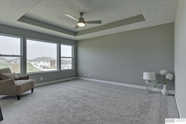 unfurnished room with a raised ceiling, ceiling fan, and light colored carpet