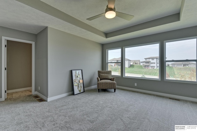 unfurnished room featuring a raised ceiling, ceiling fan, light colored carpet, and a textured ceiling