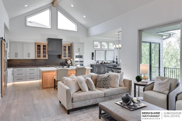 living room featuring a barn door, high vaulted ceiling, beamed ceiling, a notable chandelier, and light hardwood / wood-style floors