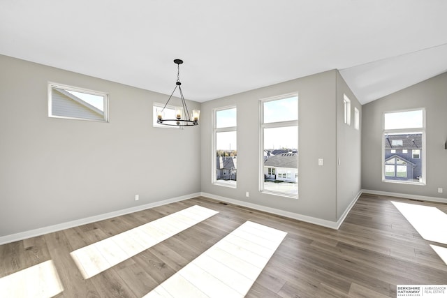 unfurnished dining area with a wealth of natural light, hardwood / wood-style floors, lofted ceiling, and a notable chandelier