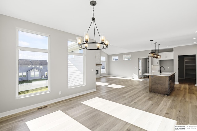 kitchen with white cabinetry, hanging light fixtures, an inviting chandelier, a kitchen island with sink, and light wood-type flooring