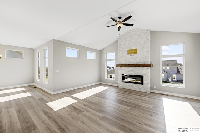 unfurnished living room featuring high vaulted ceiling, light hardwood / wood-style flooring, a stone fireplace, and ceiling fan