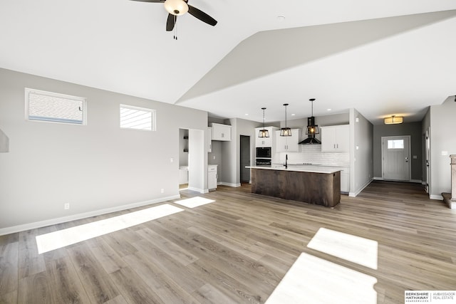 unfurnished living room featuring light wood-type flooring, plenty of natural light, ceiling fan, and vaulted ceiling