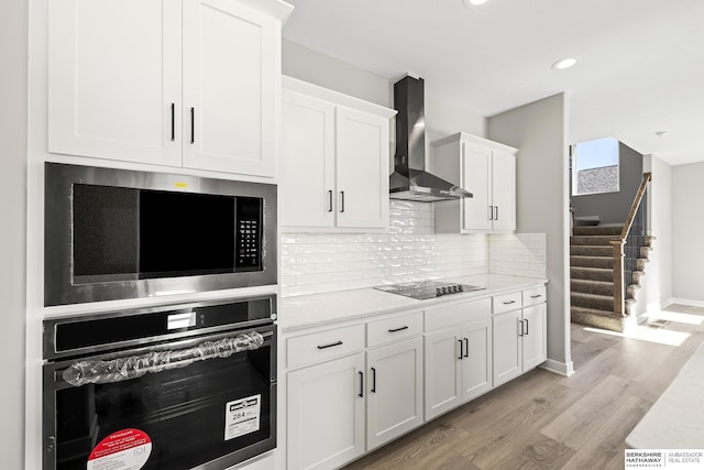 kitchen with built in microwave, stainless steel oven, wall chimney exhaust hood, black electric cooktop, and white cabinets