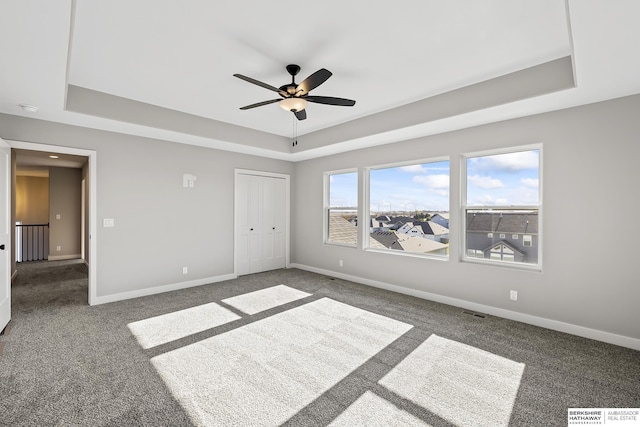 unfurnished room with a raised ceiling, ceiling fan, and dark carpet